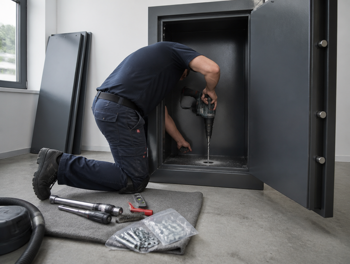 Techniker bohrt die Bodenverankerung durch den Innenboden eines geöffneten Tresors